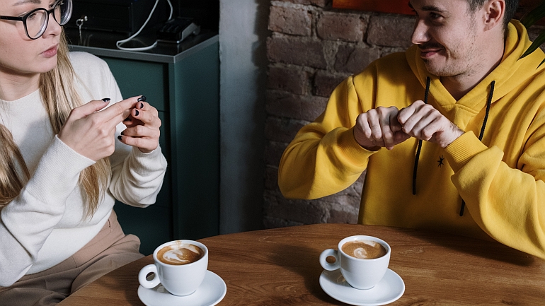 Dwoje młodych ludzi rozmawiających przy kawie przy użyciu języka migowego