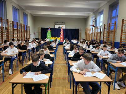 próbny egzamin óśmoklasisyty dla klas siódmych- uczniwie piszący egzamin przy stolikach na sali gimnastycznej