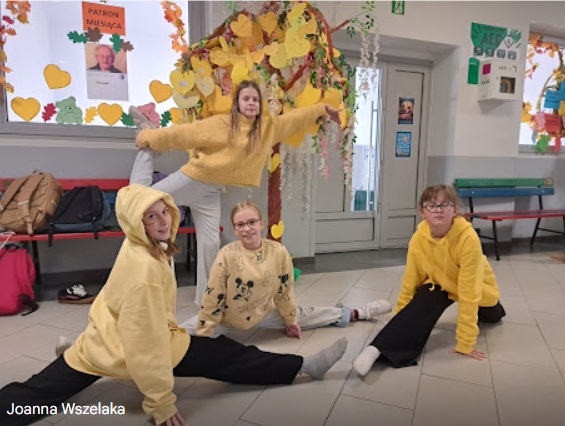 Światowy dzień życzliwości - drzewo z symbolicznymi żółtymi liśćmi i dziewczeta po drzewem ubrane w żółte kolory