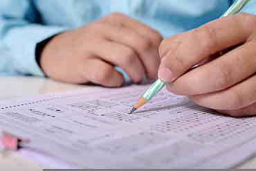 Dłoń trzymająca ołówek nad arkuszem egzaminacyjnym