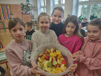Grupa dzieci trzymająca miskę z owocami przygotowanymi do wykonania napoju owocowego