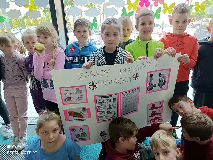 Grupa dzieci z plakatem promującym pierwszą pomoc